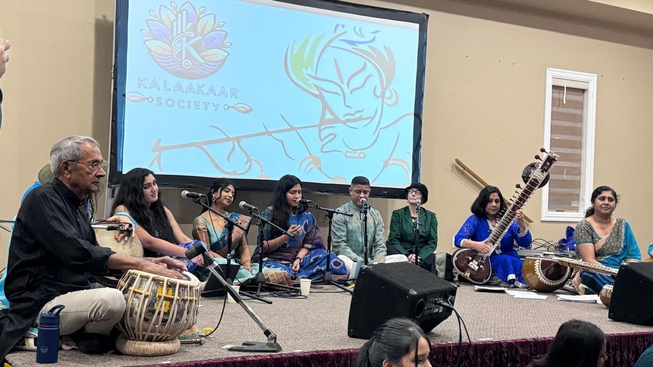 Musicians with tabla, sitar and voice performing in front of a projected Kalaakaar banner